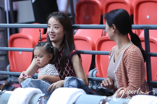 孙桐林的妻子抱着年幼的女儿端坐在观众席，母女俩专注地望向赛场方向，妻子的眼神中透露出对丈夫表现的关切。