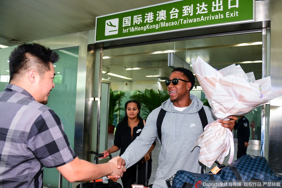 卡南将手中的鲜花递给身旁的女友，两人眼神交汇间充满甜蜜，背景是机场熙攘的人群，这一幕温情瞬间被镜头定格。