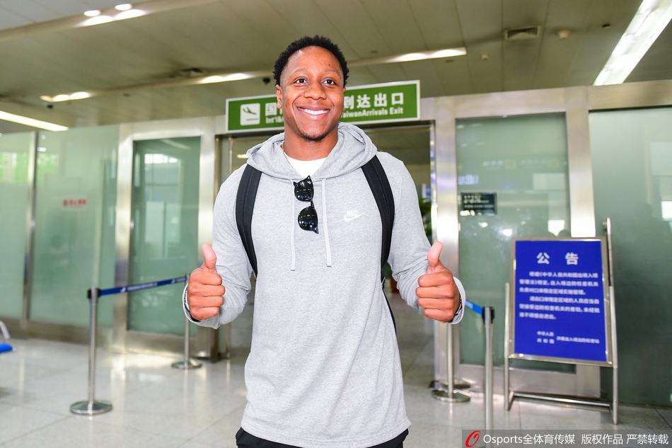 卡南在机场大厅驻足，认真地看着手机，仿佛在处理抵达后的各项事宜，身后的女友守护着行李，画面充满生活气息。