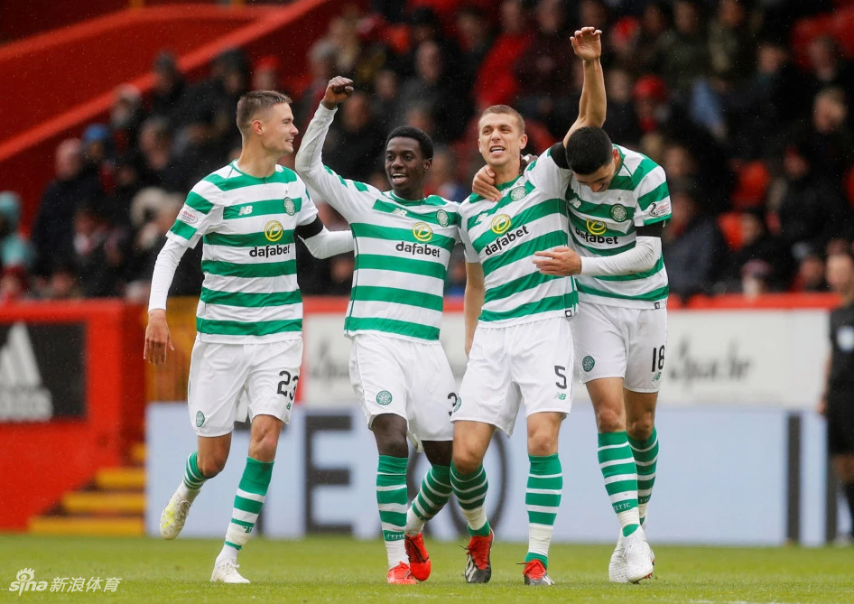 数名凯尔特人球员在草坪上围成一圈，他们互相搭着肩膀，神情专注而坚定。背景中可以看见巨大的冠军奖盘被放置在草坪中央，仿佛在激励着将士们为了下一个目标继续战斗。