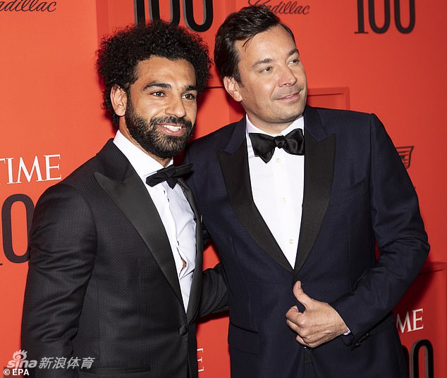 聚光灯下的萨拉赫独自站在《时代》百大人物颁奖礼的舞台上，他一手拿着奖杯，目光坚定地望向前方。深色的背景让光束聚焦在他身上，将他衬托得如同一位从历史中走来的巨人。这一刻，球场上的喧嚣远去，只留下属于思想者和榜样的宁静与力量。