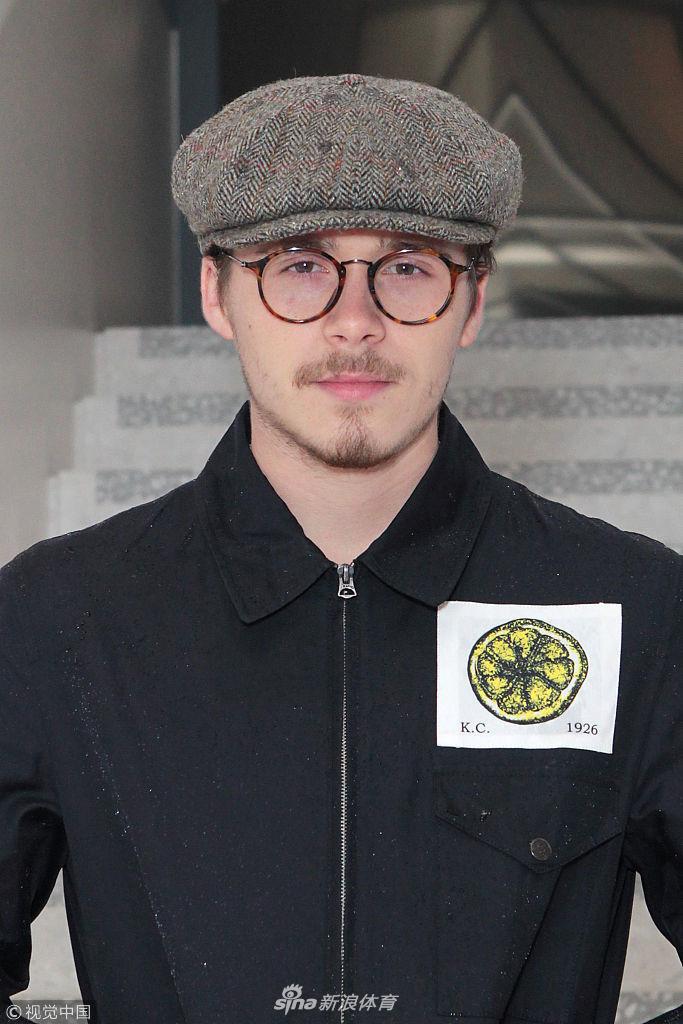 布鲁克林侧身面对镜头，略显稀疏的胡须在灯光下若隐若现，黑色报童帽压得很低，带着点倔强