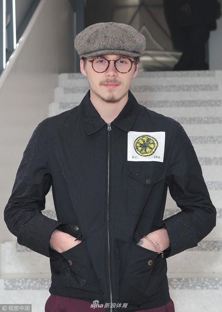 餐厅灯火辉煌的背景中，布鲁克林双手插袋，一身休闲装扮，努力摆出成熟模特的冷峻表情