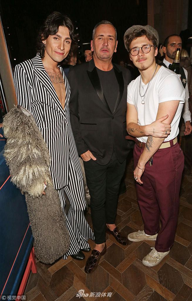 布鲁克林与友人在餐厅内交谈，脸上挂着放松的笑容，报童帽下的眼神清澈，仿佛对未来的豪门生活一无所知