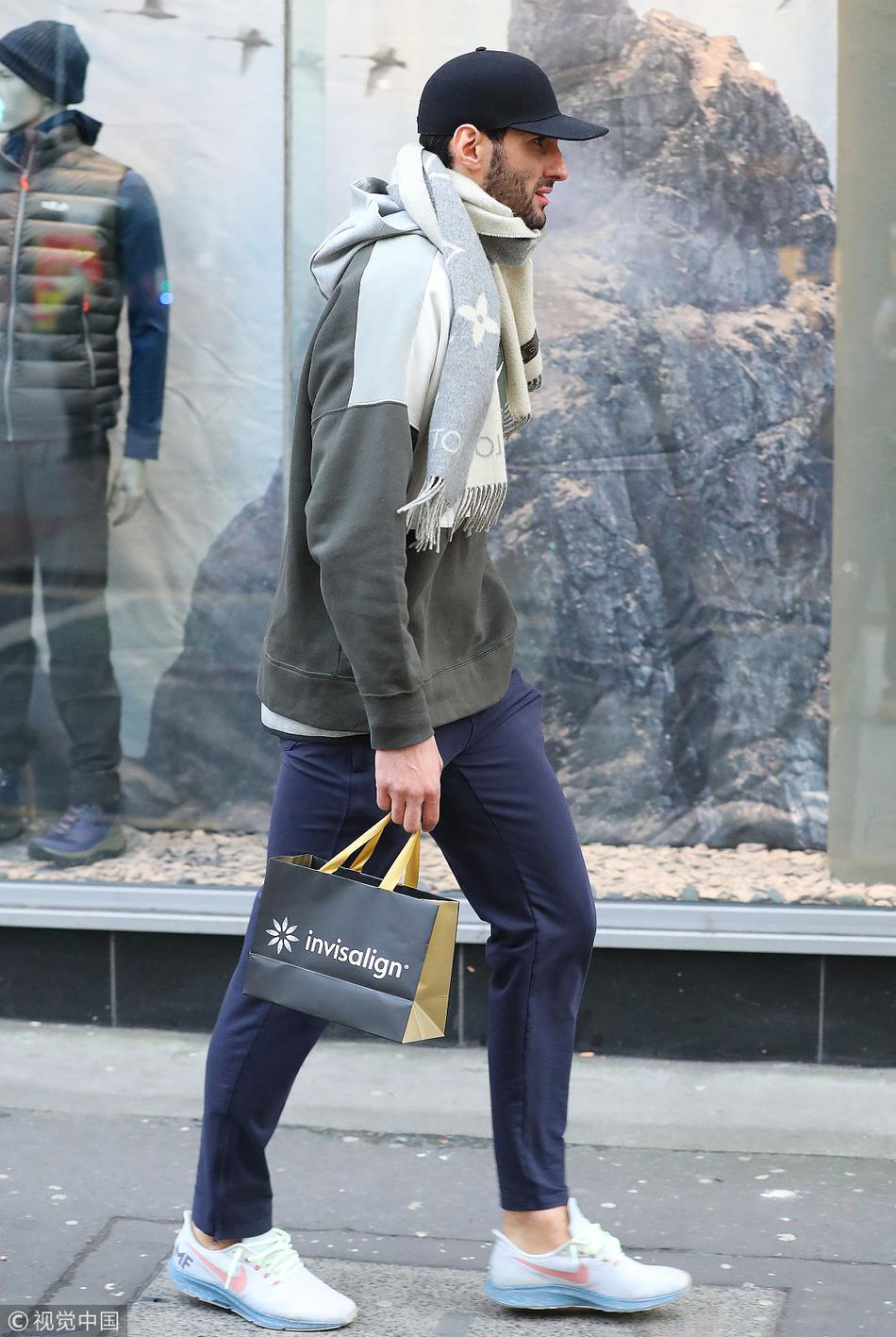 费莱尼走进一家商店，在货架前驻足停留。他侧身对着镜头，依旧穿着那件辨识度极高的羽绒服，专注地审视着商品。即便身处喧闹的商业区，他周围仿佛也被一种孤独的气场笼罩，与普通市民的日常形成鲜明对比。