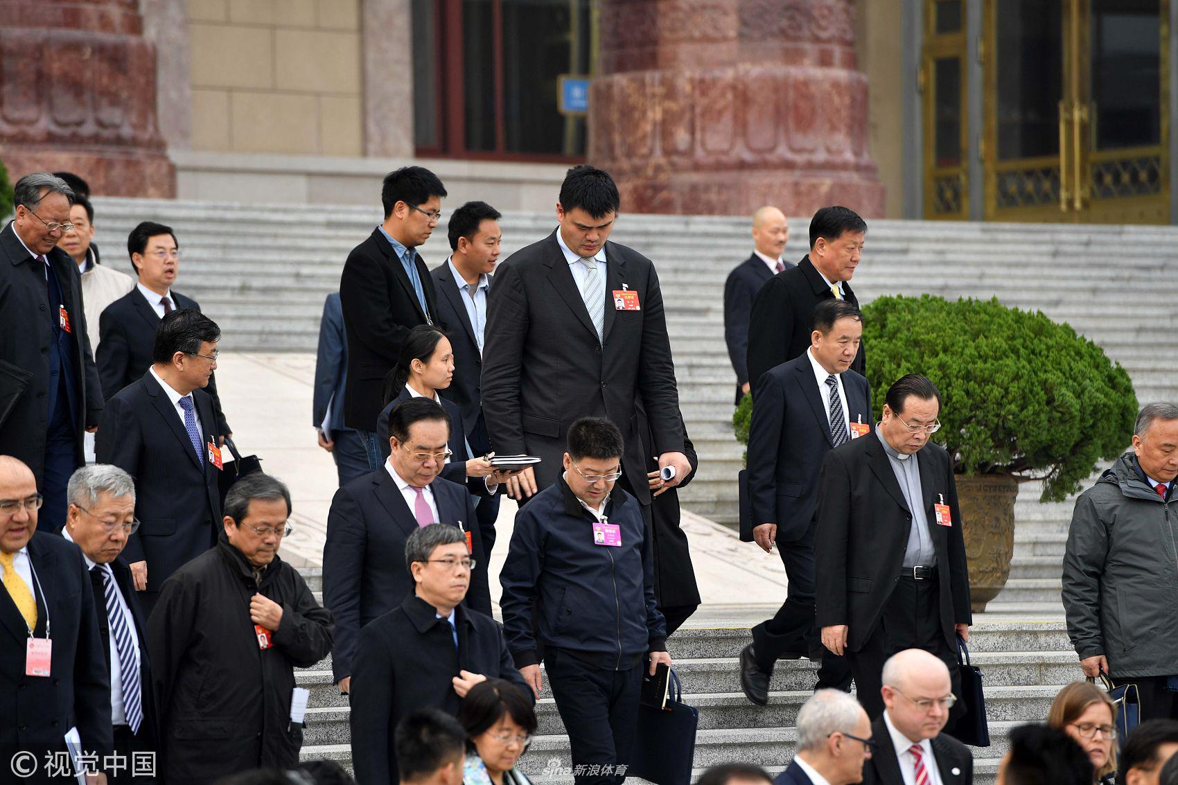 姚明在政协大会现场翻阅文件，身着白衬衫的他全神贯注于眼前的材料，背景是人民大会堂宏伟的穹顶和灯饰，这一刻，他与其他委员一样，肩负着参政议政的神圣职责。