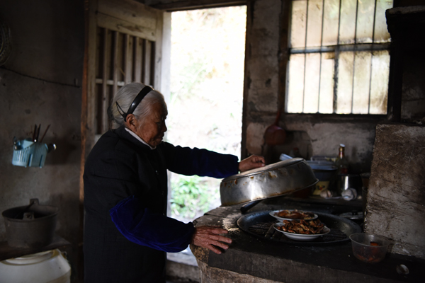 张荷仙老人给自己做早饭，把昨日所做菜品放入灶中加热。