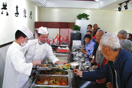 延安市宝塔区慧泽社区共享餐厅的员工给老人们盛饭菜。 本报见习记者 杨琳摄
