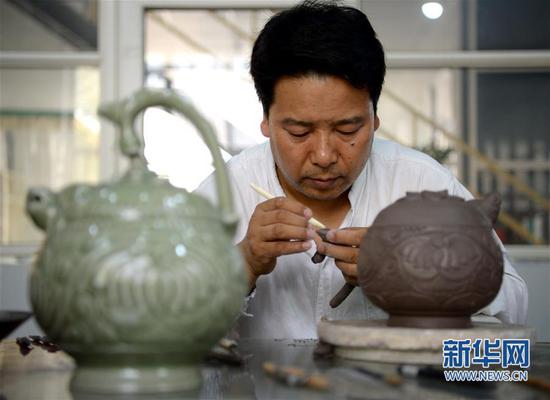 崔涛在对手工制作的耀州窑青釉剔花倒装壶进行刻花(7月10日摄)。