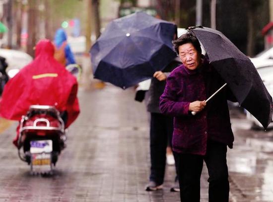 昨日西安街头，一位老人撑着雨伞艰难行走 本报记者马昭摄