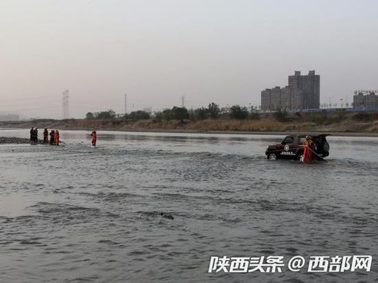 救援人員借助岸邊的一輛車將被困車輛牽引出河中。