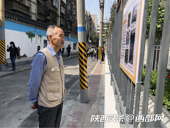 一位老人正在看新民二巷墙上的老照片。