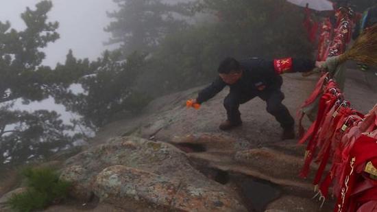 杜小利在華山西峰頂，翻越圍欄撿游客丟棄的垃圾。