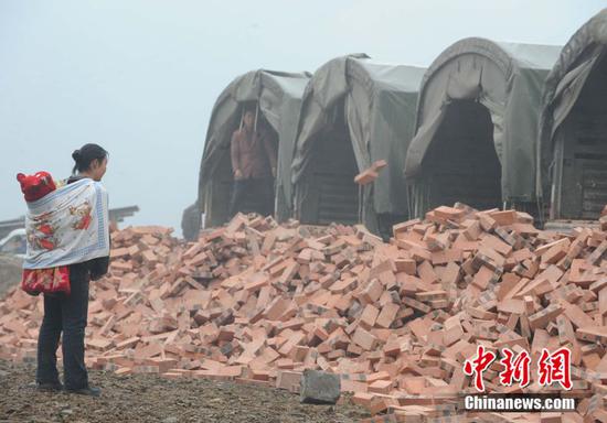 2009年1月2日，北川县一名妇女背着儿子接收解放军免费运送来的红砖，准备请人帮助重建家园。中新社记者 贾国荣 摄