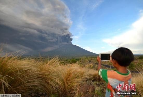 当地时间11月26日，印尼巴厘岛卡朗阿森，阿贡火山喷发。图为当地小朋友淡定拍照。  