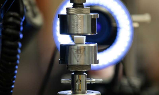 一块取自墨鱼骨的立方体状样本被放置在用于压力测试的机械测试台上。图片来源：Peter Means for Virginia Tech