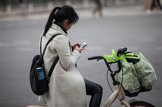 一名行人骑车间隙还在玩手机。视觉中国 资料