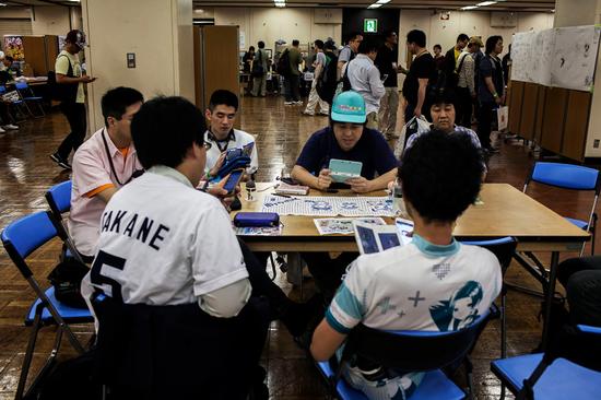 日本恋爱游戏:这些日本玩家只愿跟游戏角色谈恋爱 在东京一场活动中,《爱相随》玩家拿着游戏机围桌就坐。图片来源:LOULOU D’AKI