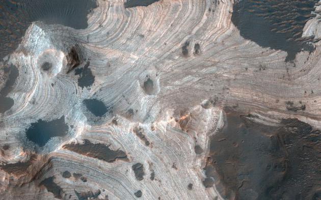 这张照片是由美国宇航局火星勘测轨道飞行器(MRO)机载高分辨率科学实验成像相机(HiRISE)拍摄的，呈现出直径140公里的霍尔顿陨坑中存在漩涡层状砂岩。