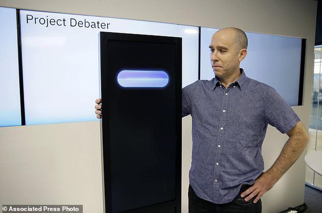 图为首席研究员诺姆•斯洛尼姆站在人工智能机器Project Debater旁边。该机器即将在接下来于旧金山展开的辩论赛中与两名人类对决。斯洛尼姆在程序中加入了幽默元素，但机器有时会在不合适的时机开玩笑。