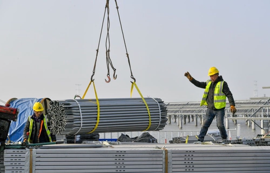 ↑在天津滨海新区龙源海晶盐光互补项目建设现场，建设者指挥吊运光伏板结构组件（2月7日摄）。