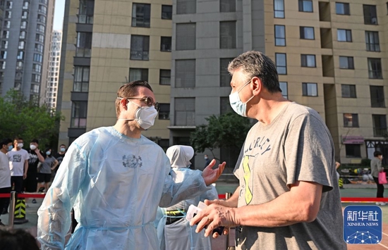 5月22日，在天津市南开区时代奥城社区核酸检测点，李翰文（左）和前来进行核酸检测的外籍人士交流。新华社记者 赵子硕 摄