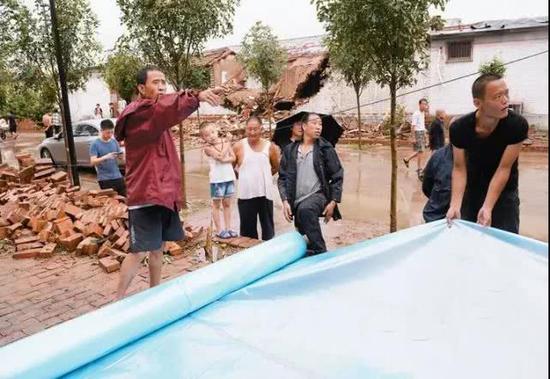 村委会成员和村民一起用防雨罩遮挡损毁设施。
