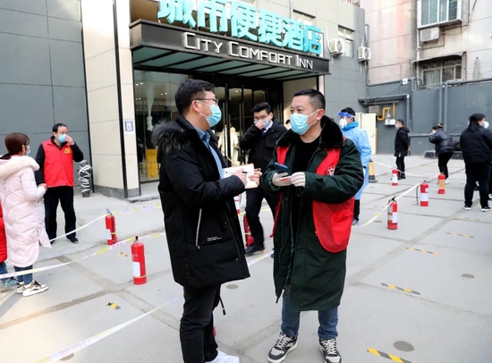 2022年1月15日,郑州对重点区域进行第8轮全员核酸检测。人民日报社河南分社记者毕京津(左)在位于郑州市金水区丰产路街道的城市便捷酒店全员核酸检测点,采访参加核酸检测的医务工作者、社区工作人员和志愿者。