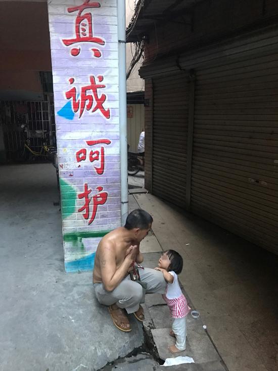 王忠馗和七女儿在家门口,身后是邻近幼儿园的彩绘,写着“真诚呵护”。