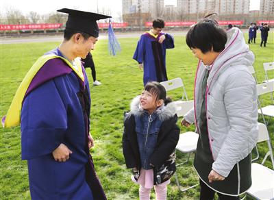 一名山东毕业生的母亲带着7岁小女儿参加大儿子的毕业礼。