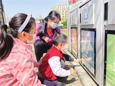 李品媛和孩子跟智能垃圾箱“小智”互动。（照片由生态城提供）