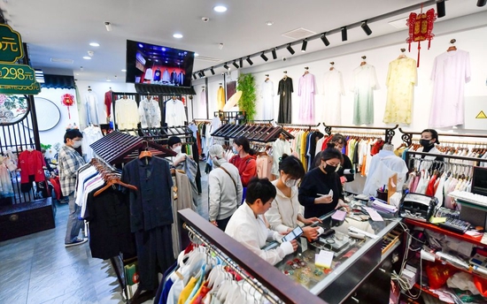 ↑4月29日,游客在天津古文化街一家服装店购物。
