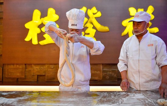 在天津桂发祥十八街麻花文化馆，徒弟赵宝阳在王洪德（右）的指导下搓制手工麻花（6月8日摄）。