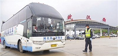 图：3月24日，在武汉西高速收费站交通卡点，执勤民警准备检查车辆。新华社发