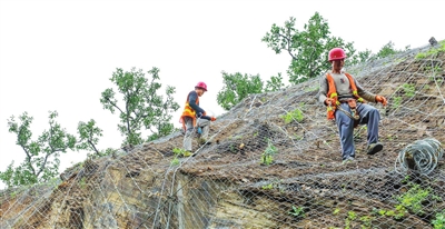 图为津围公路沿线，施工人员对山体增设防护网。