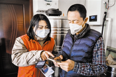图为工组人员向村民发放安全用电知识读本,讲解“煤改电”电价政策。