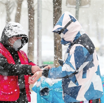 纪明家园社区的党员志愿者在大雪中对进入小区的居民测量体温。