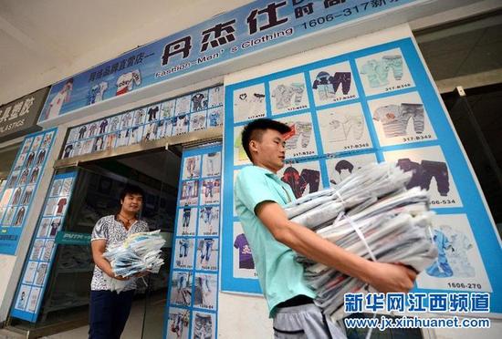 7月25日,在新余市高新区网店一条街,一家服装店主在仓库搬运网上交易成功的衣服。