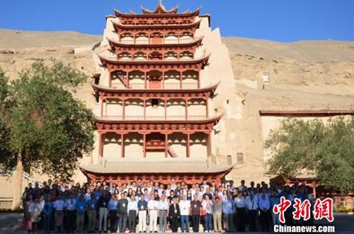 参会的专家学者在莫高窟标志性建筑“九层楼”前合影留念
