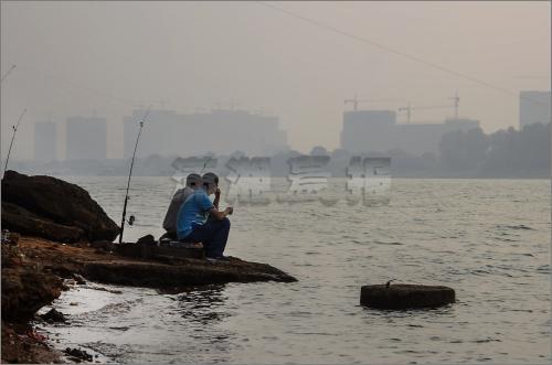 10月6日，长沙猴子石大桥附近，男子在江边钓鱼，对面的建筑若隐若现。图/实习生陈明谋记者蒋丽梅