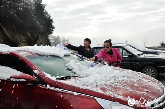 2014年11月25日，在湖北省保康县马桥镇尧治河村委会广场上，两名女士正在扫去车上的积雪。