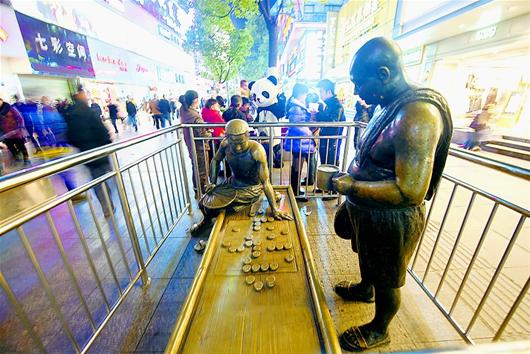 图 为：昨日，武汉市江汉路步行街，冰冷的铁栏杆将另一代表性的公共文化雕塑下棋老翁与熙熙攘攘的人流隔开，邻近的玩偶“熊猫”却吸引了大批人群的围观。 　　(记者 孙文 摄)