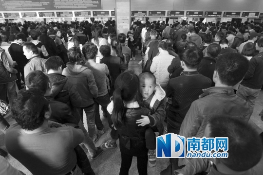 18日在广州站售票厅，买票队伍排到大厅门口，一位母亲抱着孩子站在队伍里。南都记者 马强 摄