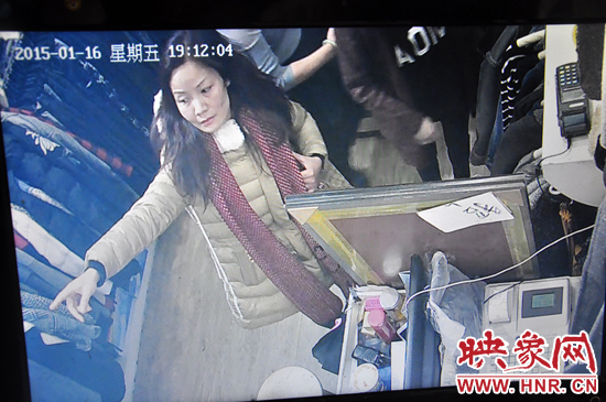 女子靠近收银台，指着墙上挂着的衣服，转移店员的注意力。