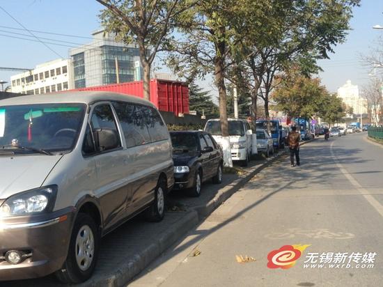 贡湖大道人行道板上停满了车,行人只好在非机动车车道上行走。