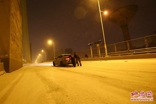 雪天路滑，汽车上桥打滑，两名“推车人”帮助一辆私家车上坡。