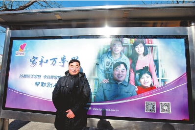 李高峰在北京街头“首都最美家庭”宣传片前留影纪念。