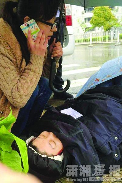 4月7日,中南大学升华学生公寓附近,秦丹丹用手机拨打电话,另一只手撑伞为晕倒女子挡雨。之后陆续有路人前来帮忙,直到救护车到来。