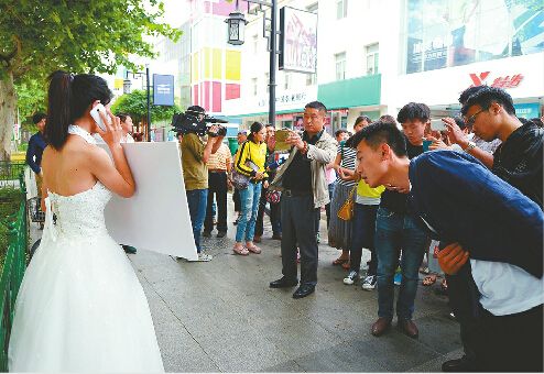 14日下午1点半，范丕英穿上买来的二手婚纱，上街继续举牌征婚，围观的市民不少，但愿意提供帮助却没有，接到电话中有一半以上是质疑和骚扰。