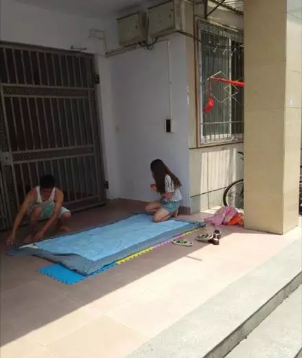 信阳师范学院某宿舍楼下,一对情侣蹲在宿舍门口,地上铺着一床展挺的图片